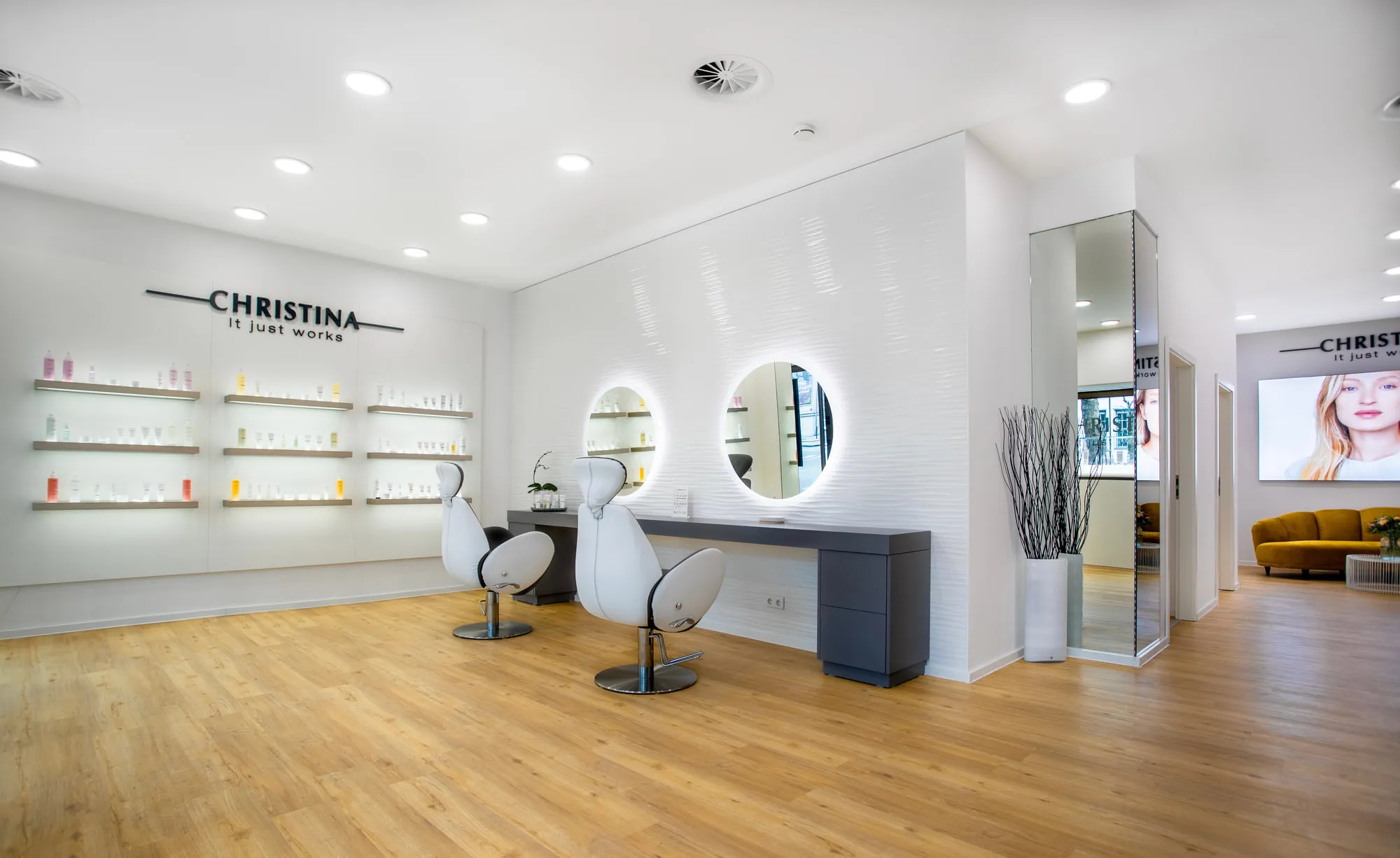 Christina Kassel — the finished salon: oak floor, product wall and backlit round mirrors