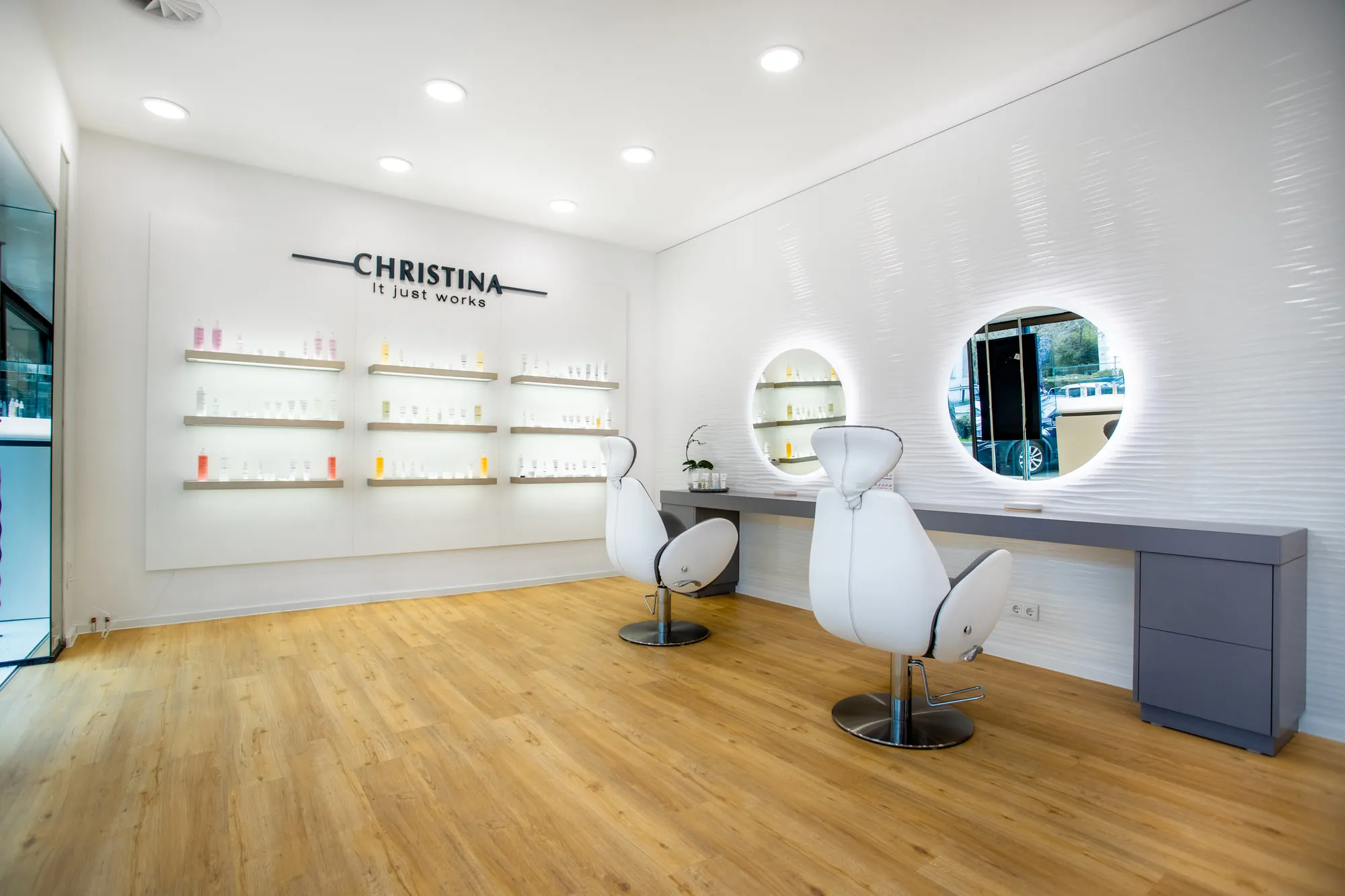 Christina Kassel — the finished salon: oak floor, product wall and backlit round mirrors