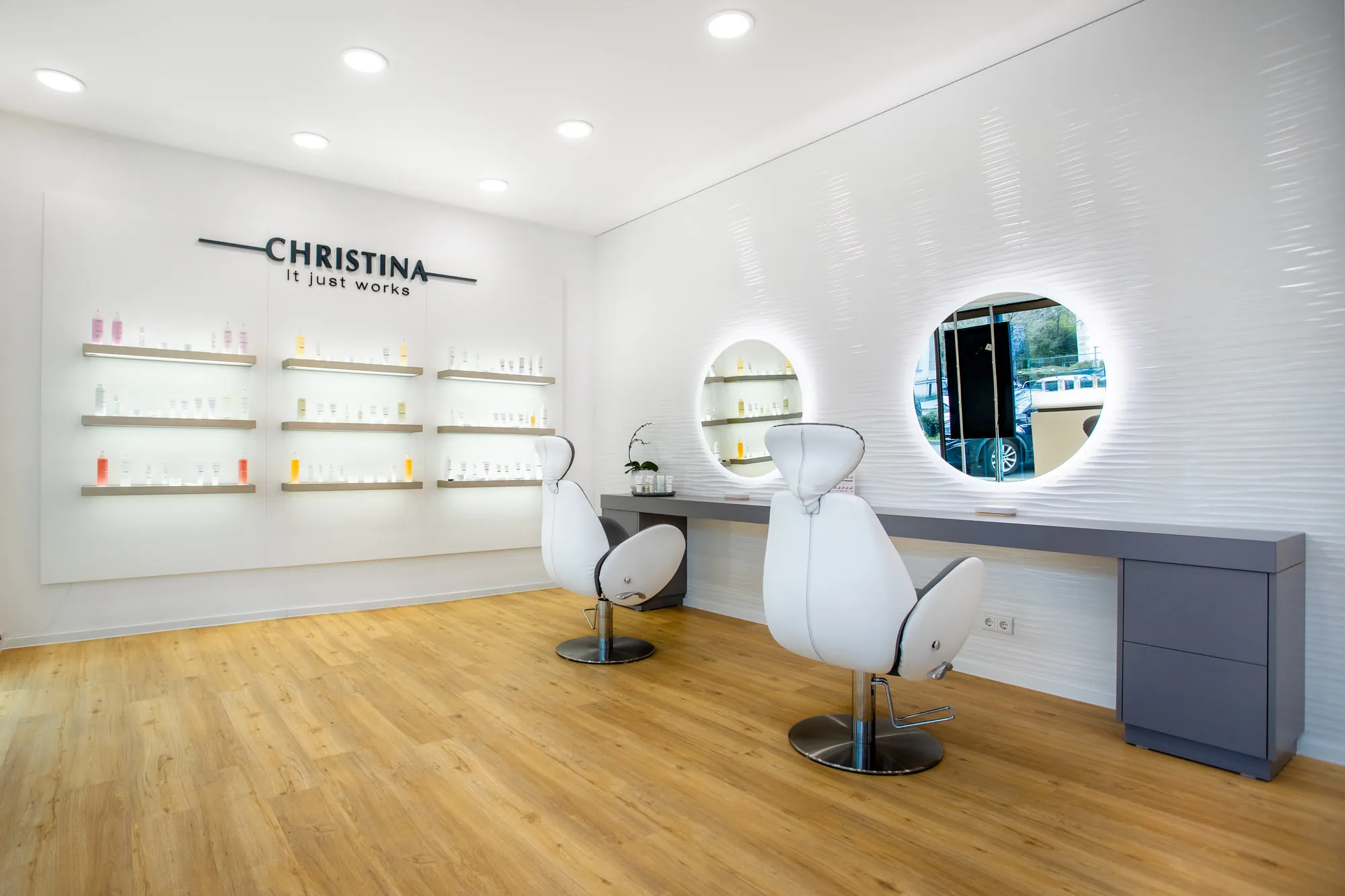 Christina Kassel — the finished salon: oak floor, product wall and backlit round mirrors