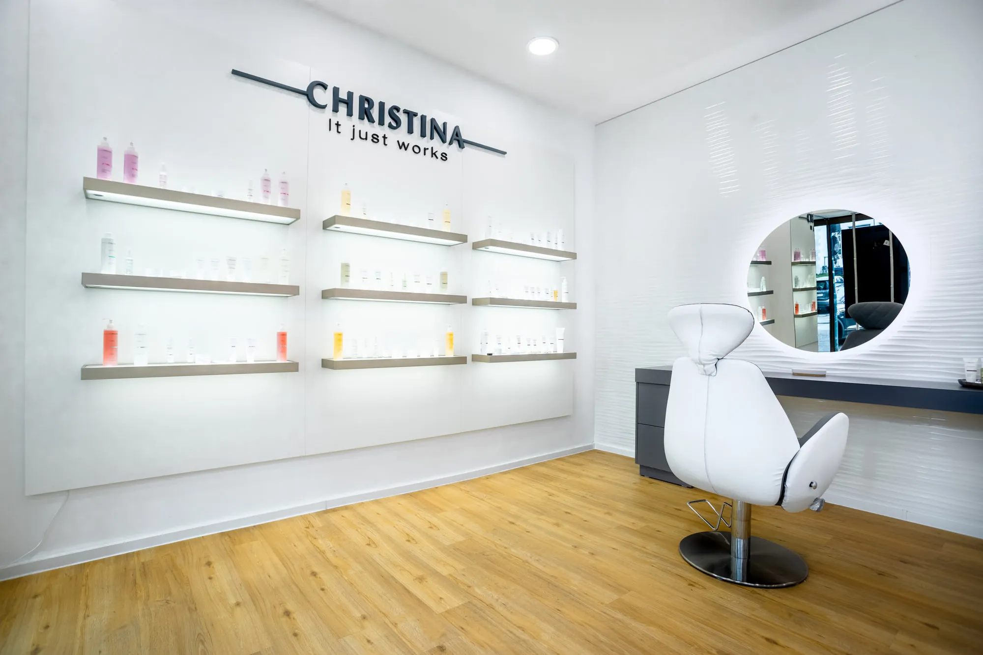 Christina Kassel — the finished salon: oak floor, product wall and backlit round mirrors