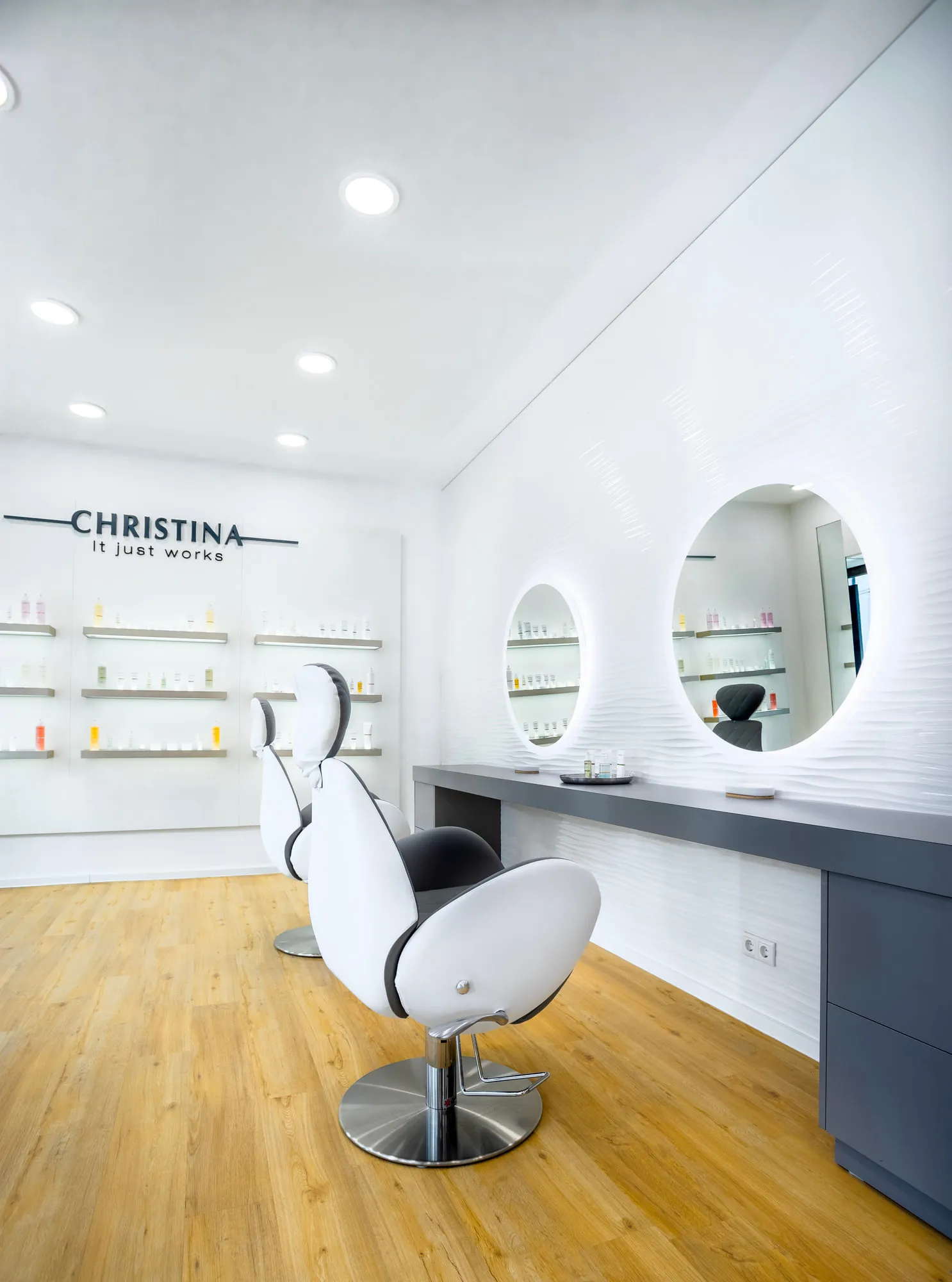 Christina Kassel — the finished salon: oak floor, product wall and backlit round mirrors